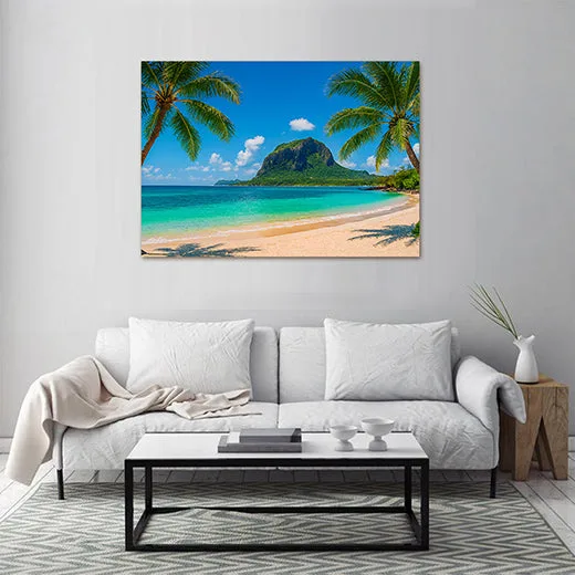 Kunstdruck Palmenstrand Felsen III – Hinter einer weiten, flachen Bucht mit sanft auslaufenden Wellen ragt ein massiver, grün bewachsener Berg auf, flankiert von zwei Palmen und einem sonnenwarmen Sandstrand